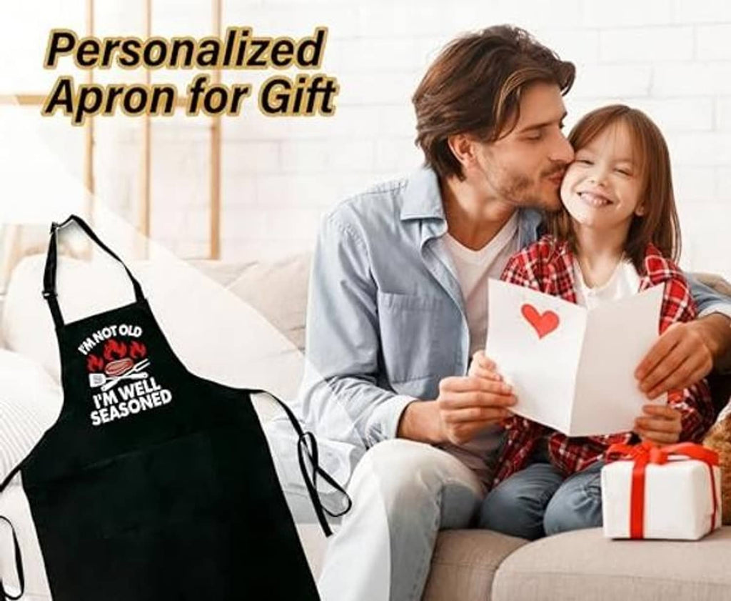 Black cooking apron with printed message and utensil icons, adjustable neck and waist ties