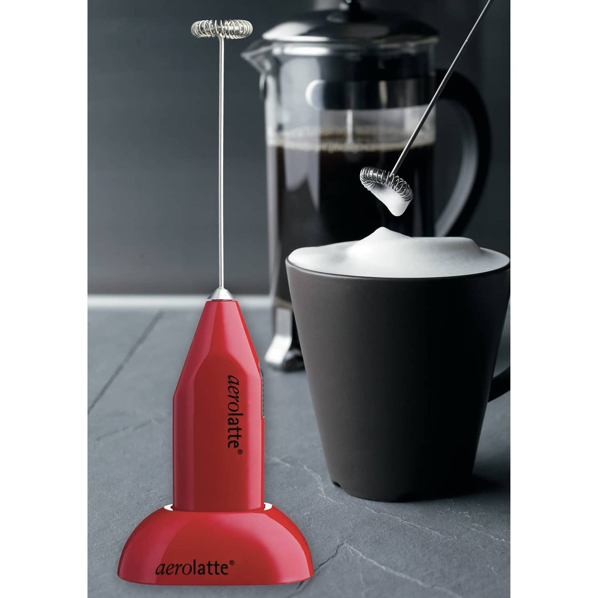 Red milk frother on counter stand next to frothing container