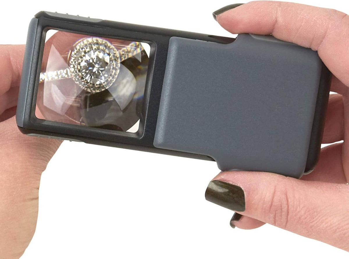Handheld gray LED magnifier displaying a magnified diamond ring through lens