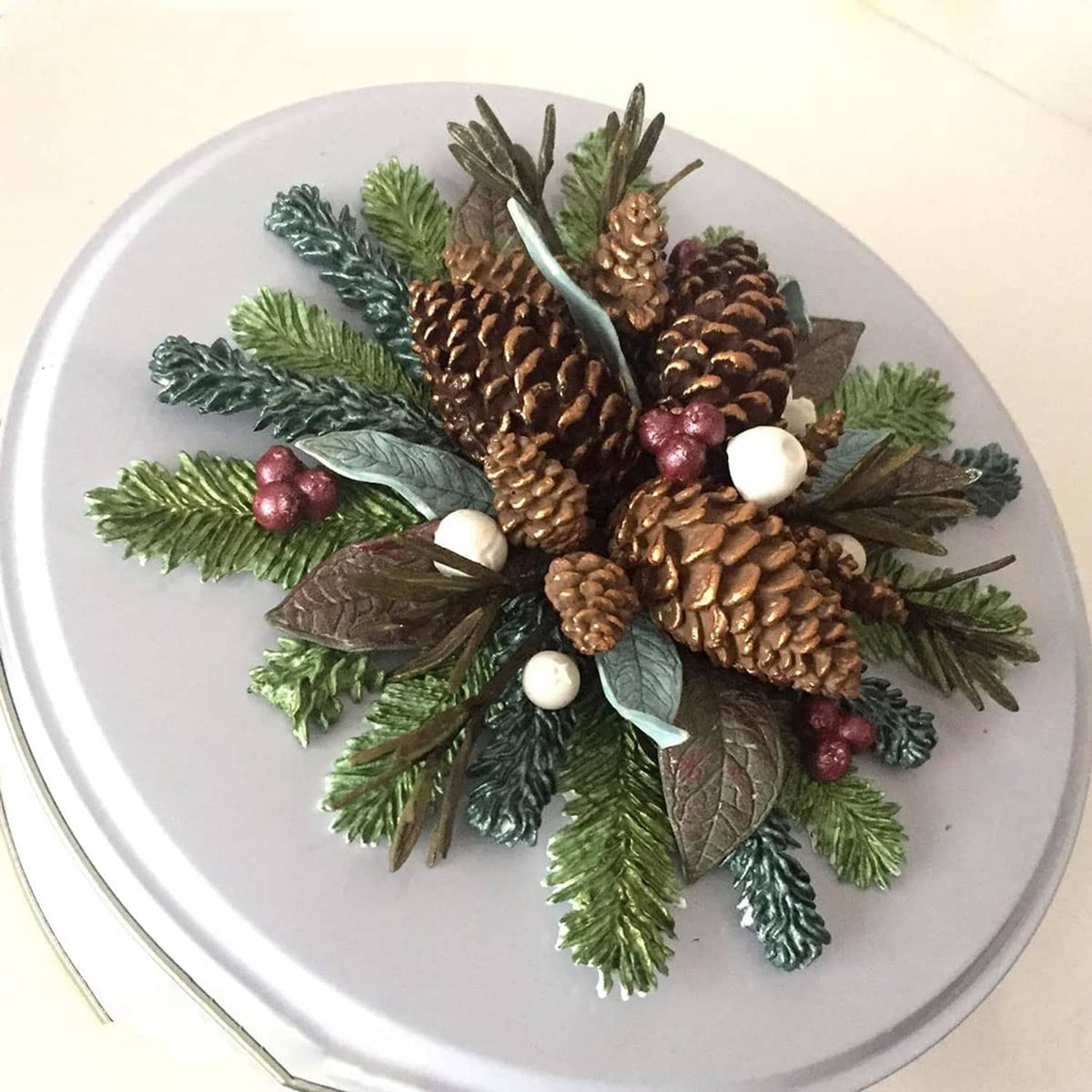 Winter foliage cake topper with pinecones, berries, and mixed green leaves