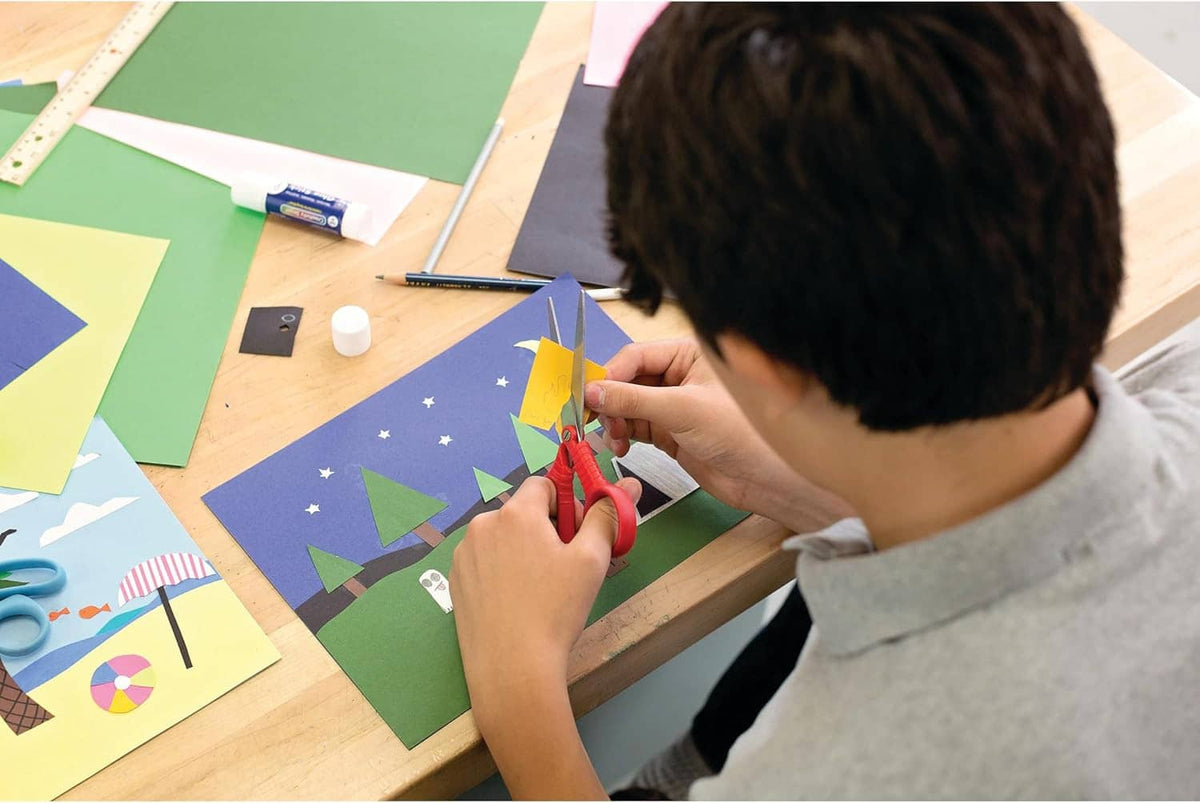 Hands cutting colorful construction paper shapes on a worktable with scissors