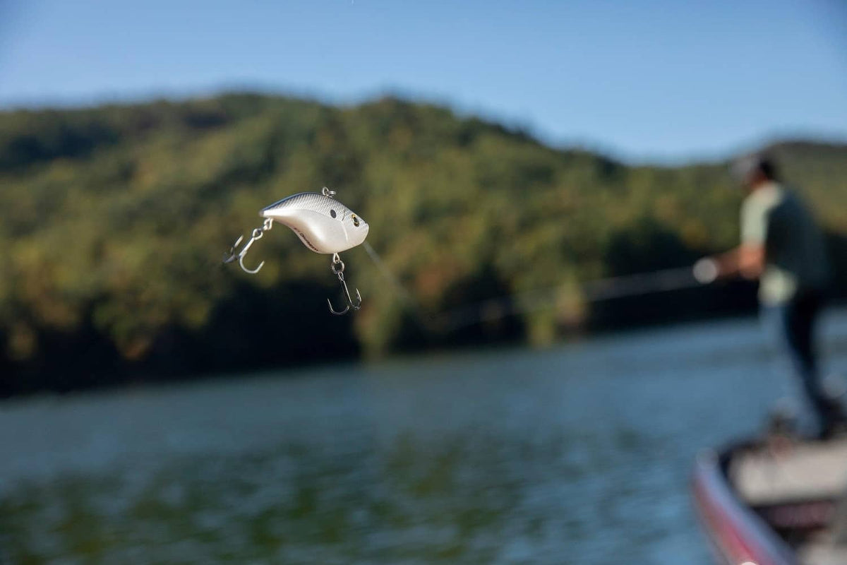 White crankbait suspended on fishing line with treble hooks near shore