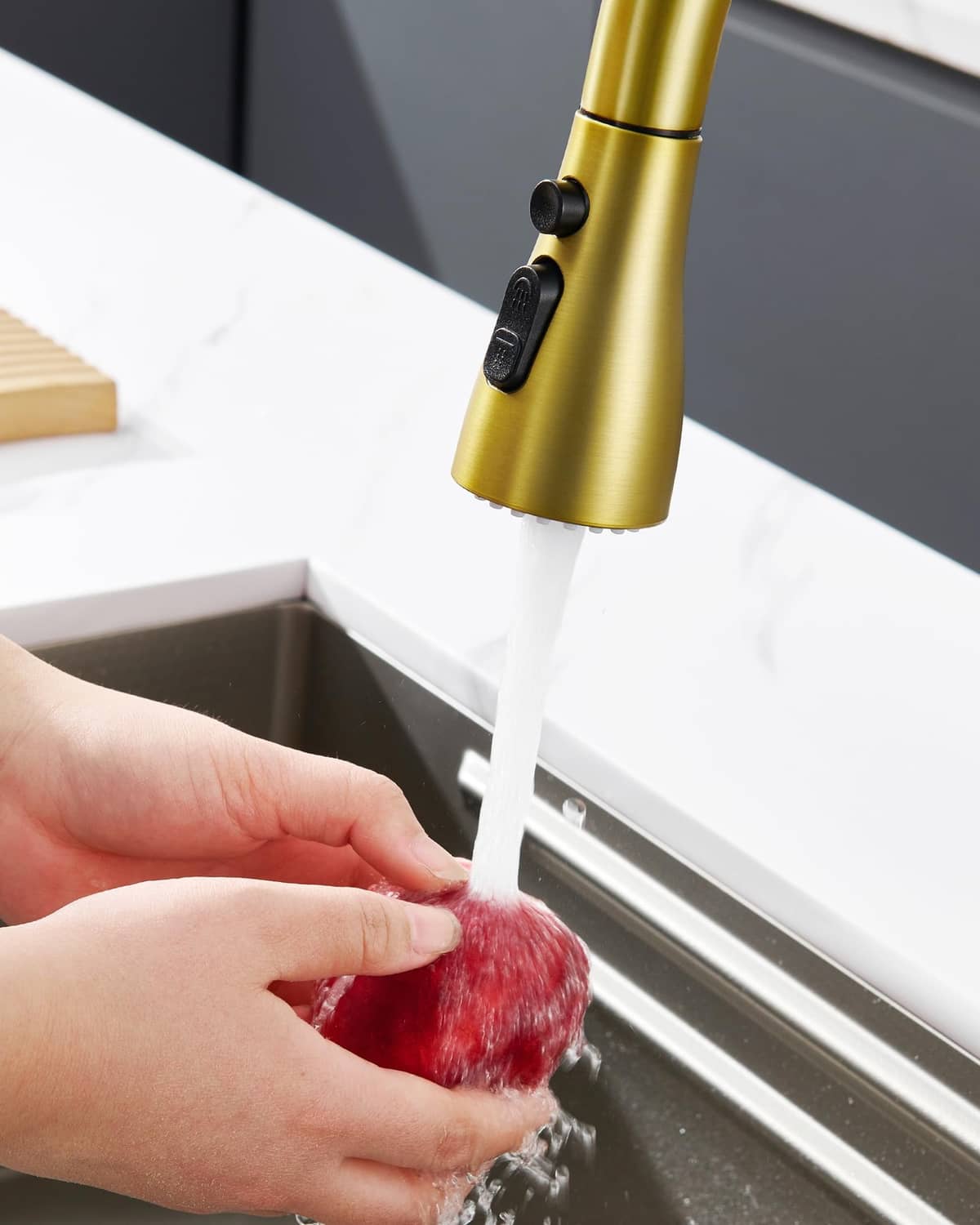 Brushed gold pull-down sprayer head dispensing water onto sink surface