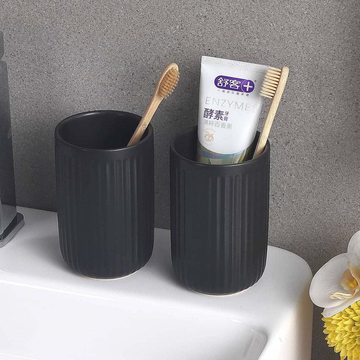 Pair of matte black ceramic toothbrush holders with ribbed sides and two toothbrushes