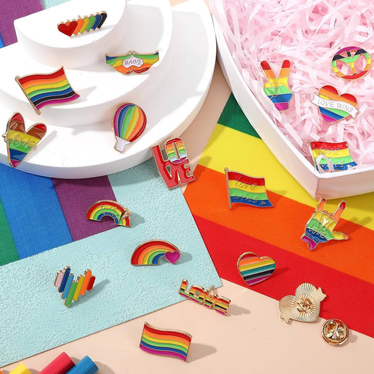 Close-up of assorted rainbow Pride enamel pins with rainbows, hearts, and heart hands.