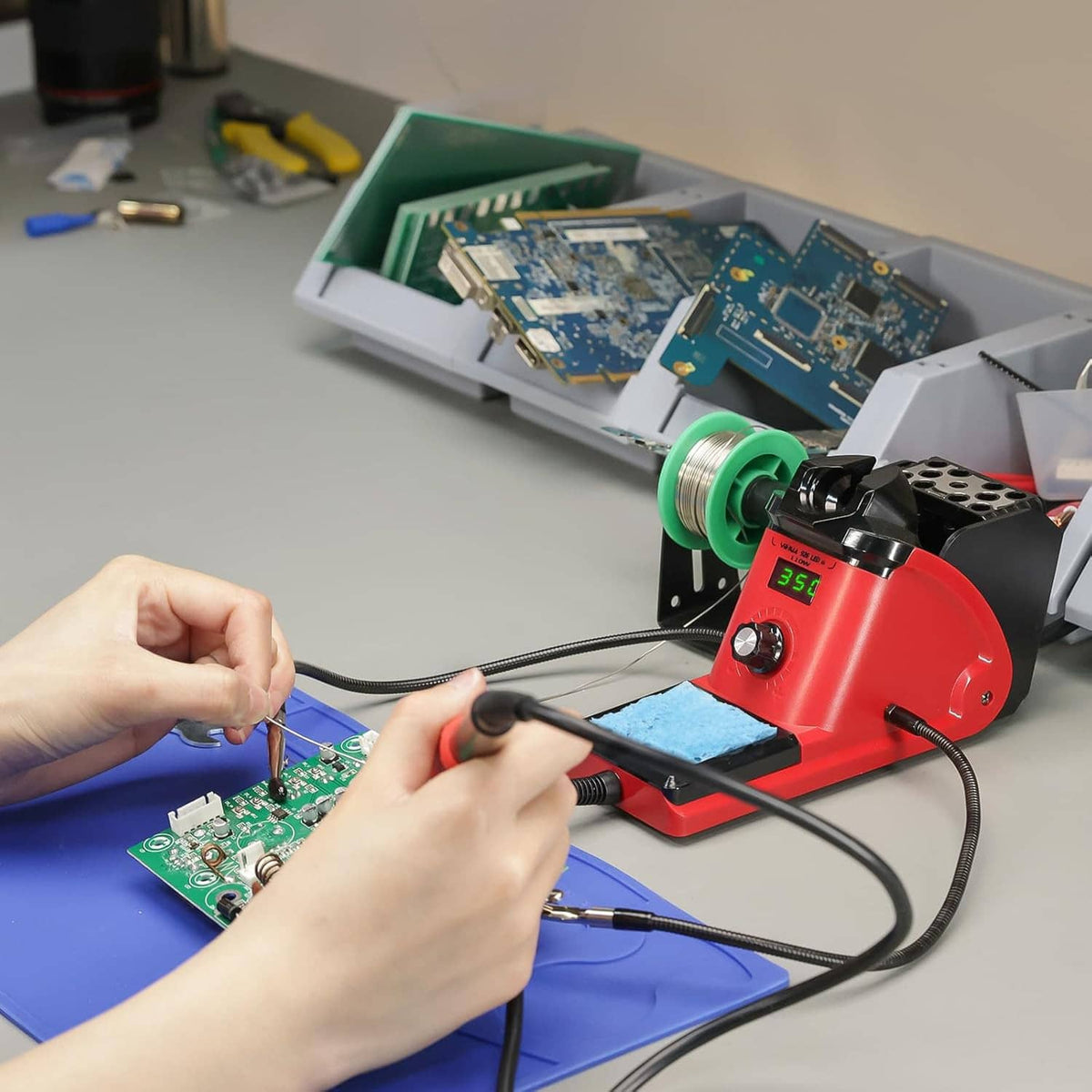Hands soldering a circuit board using a soldering iron next to the station and sponge