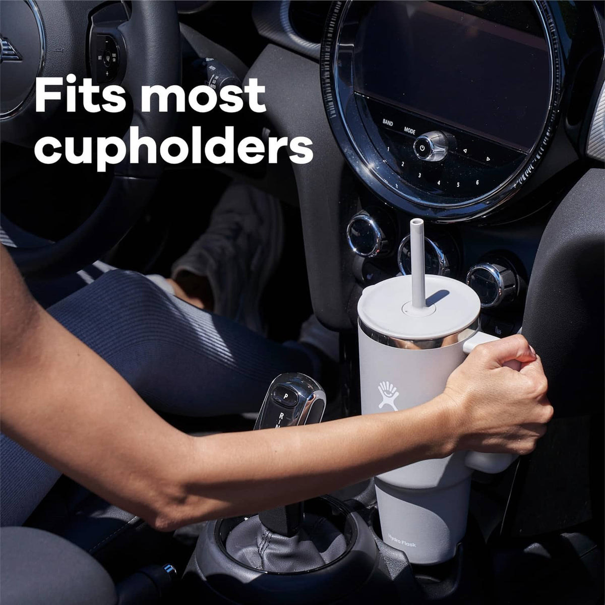 White travel tumbler with straw, handle, and lid placed in a car cup holder.
