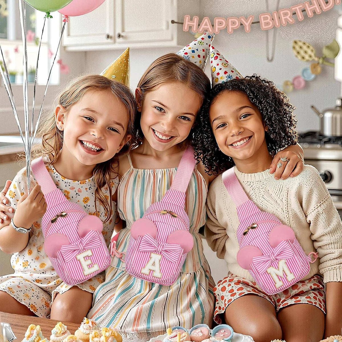 Three girls smiling while wearing pink striped sling bags with bows and letters