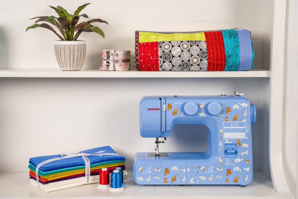Blue Janome sewing machine on a shelf, with cat decals and top dials