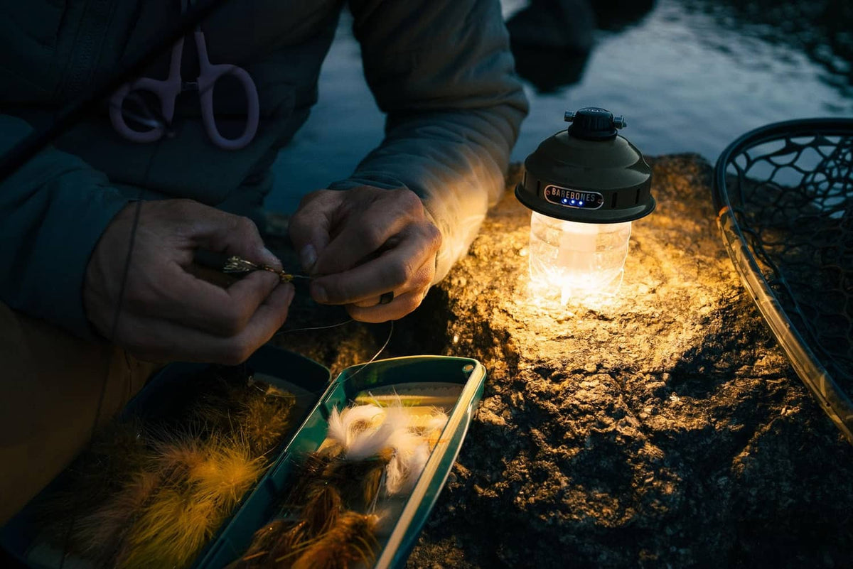 Warm-lit LED camping lantern on ground near gear, olive drab with carry handle