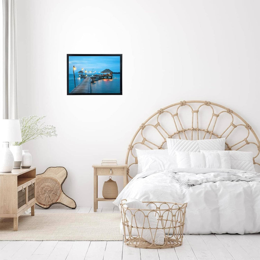 Single black photo frame hanging on a bedroom wall above a bed with white bedding