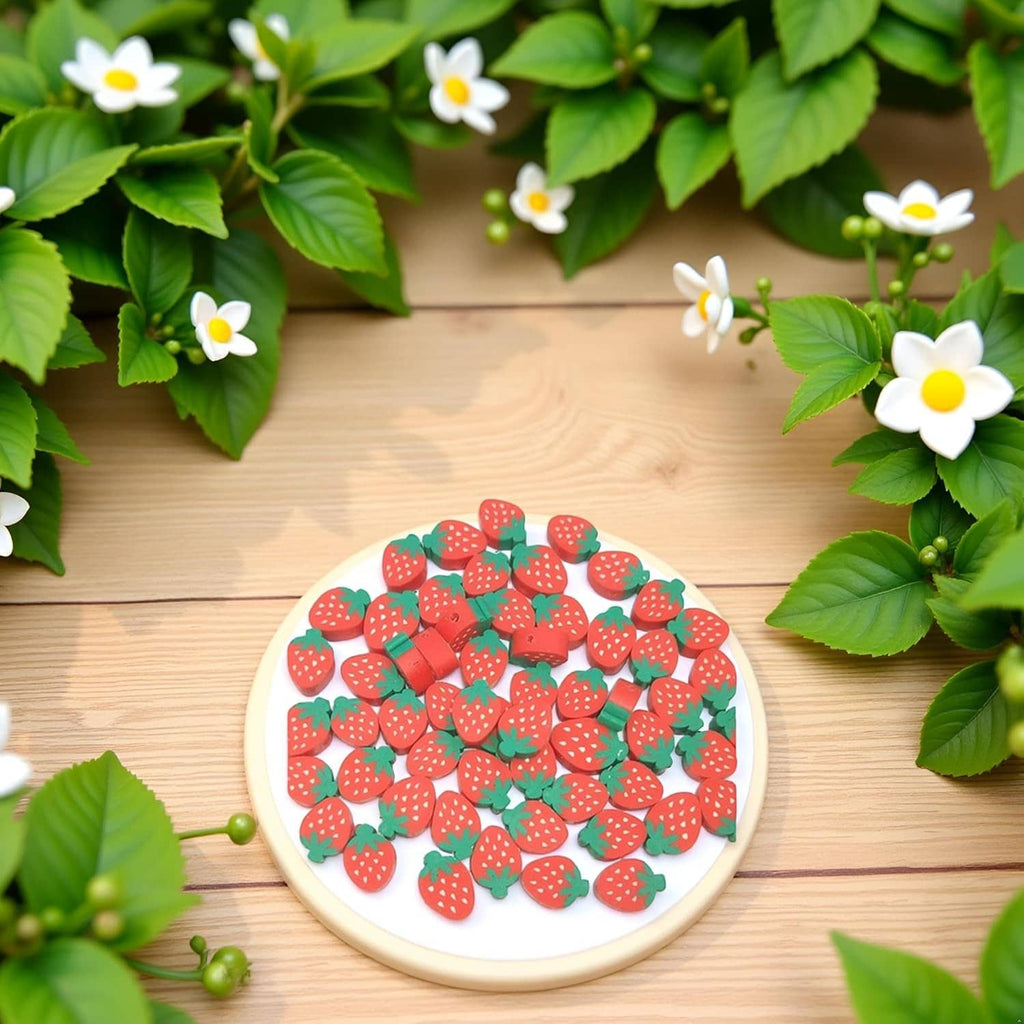 Strawberry-shaped polymer clay beads in a round dish, red fruit with green leaves.