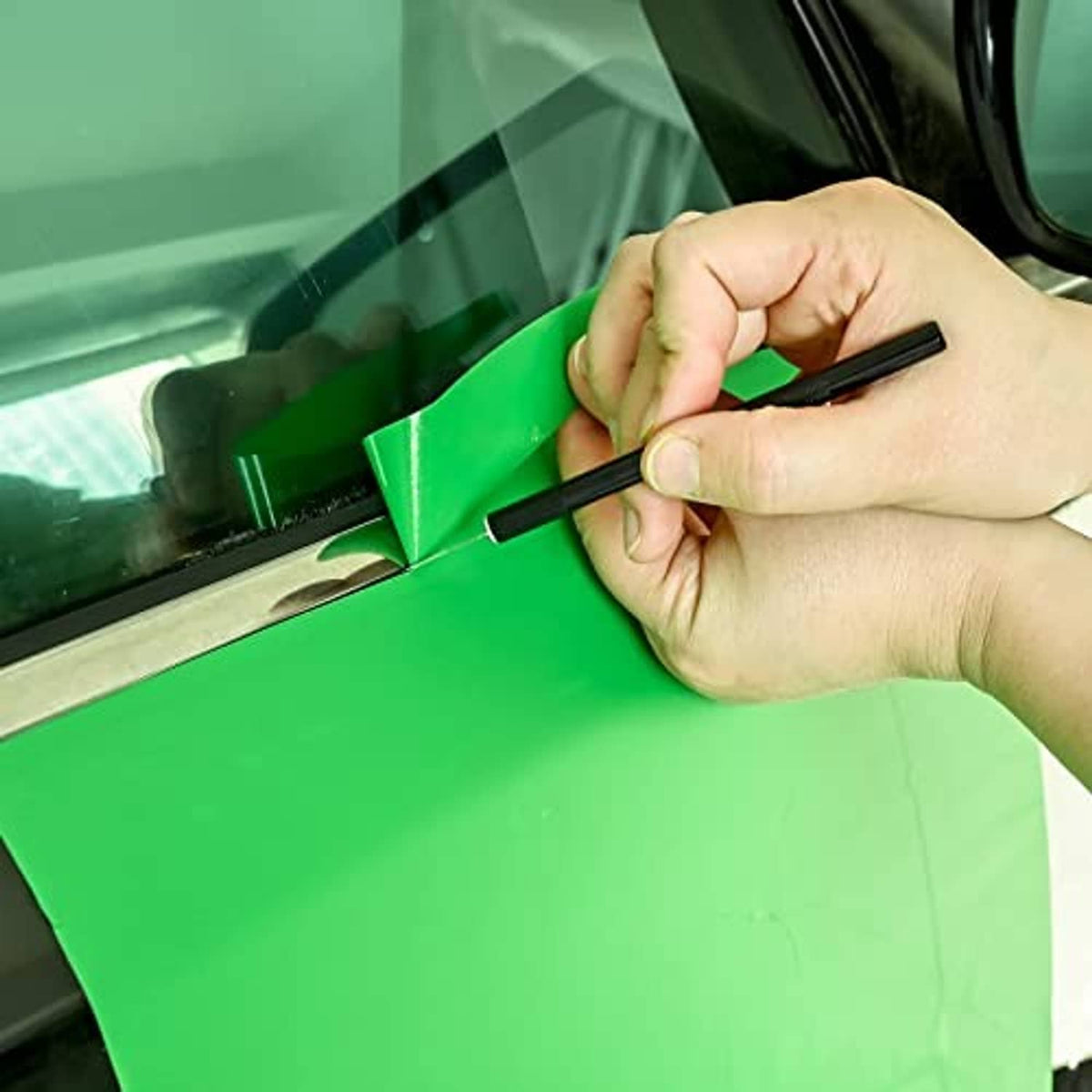 Hand smooths green window film with felt squeegee and black craft knife