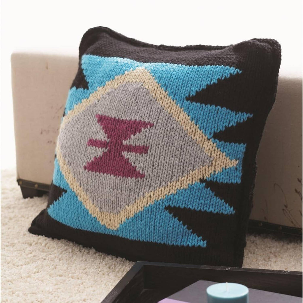 Knit pillow cover in dark yarn with blue diamonds and gray logo patch