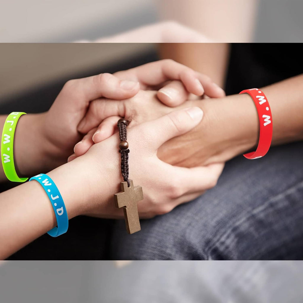 Hands wearing colorful silicone wristbands with white lettering and a wooden cross charm