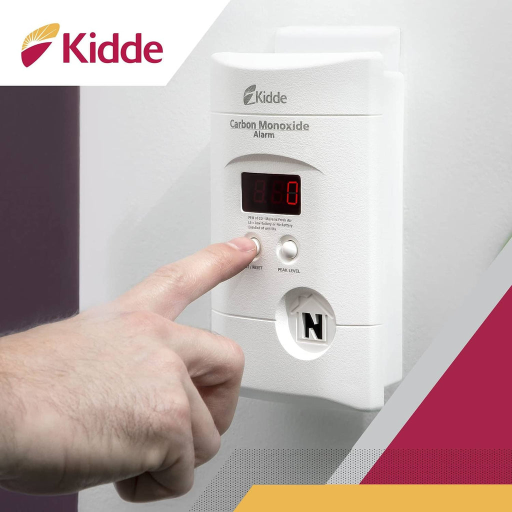 Kidde white carbon monoxide alarm with red screen; hand pressing test/reset button