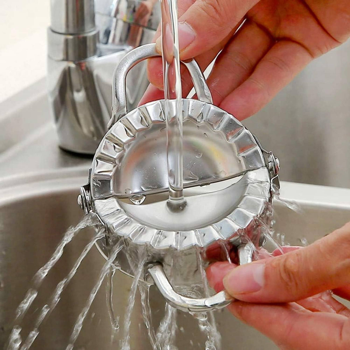 Stainless steel dumpling press with handles rinsed under running water in a sink