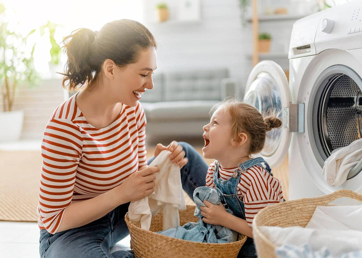 Laundry day: mother and child placing clothes into a front-load washing machine