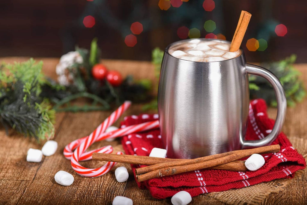 Stainless steel insulated coffee mug with handle, filled with hot drink and cinnamon stick