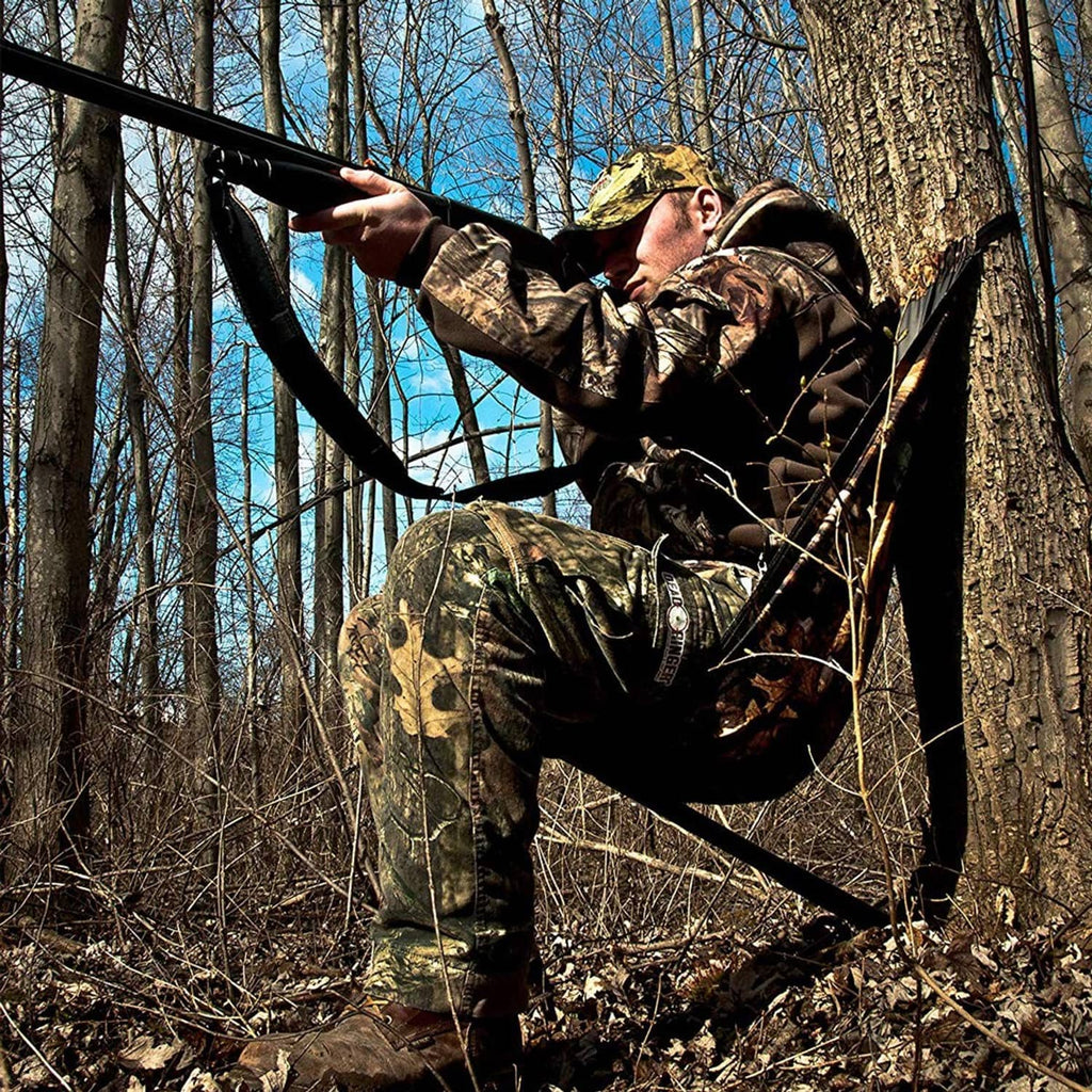 Camouflage hammock-style camping chair with black suspension straps around a tree