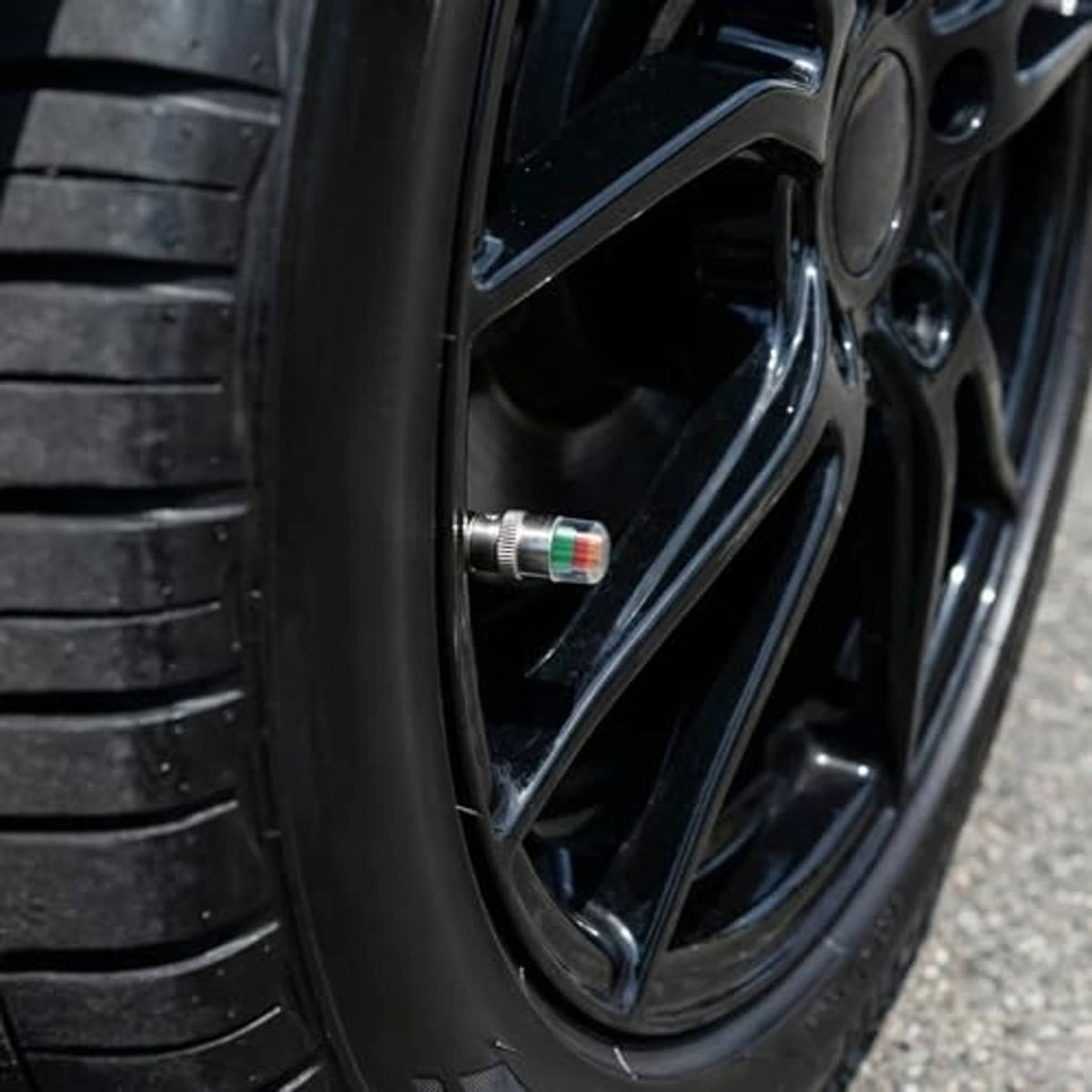 Tire valve cap installed on black wheel, silver metal with multicolor indicator insert