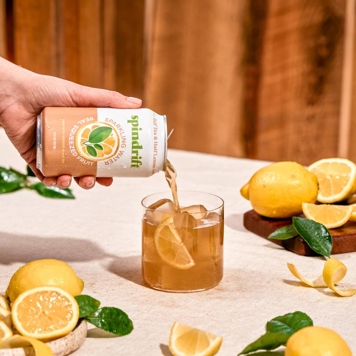 Hand holding half tea & half lemonade sparkling water can beside a glass with ice