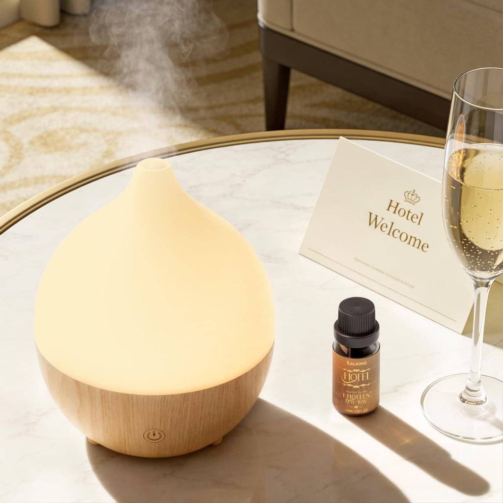 Droplet essential oil diffuser on a tabletop with included hotel welcome scent oil bottle
