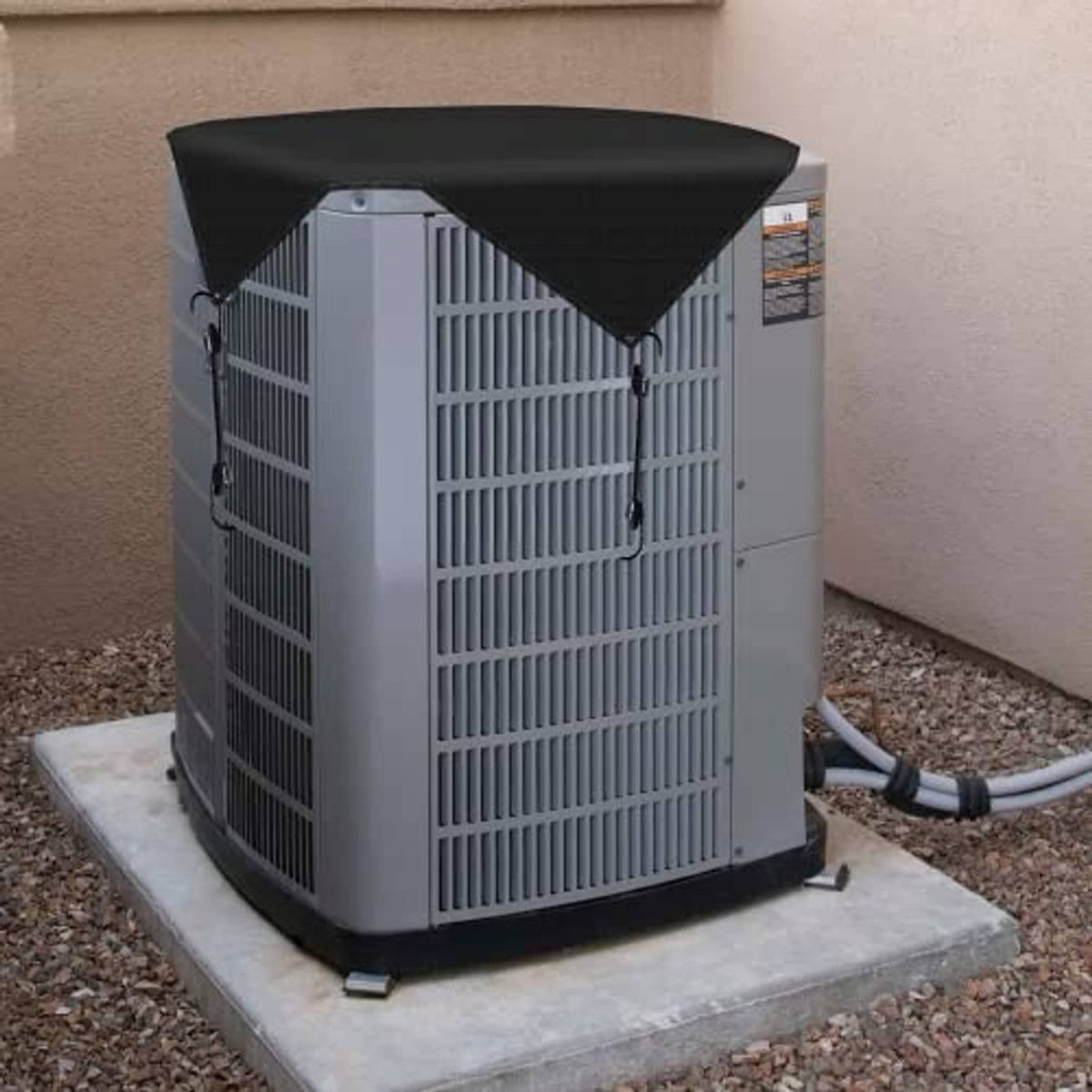 Waterproof vinyl AC unit cover on outdoor AC compressor, black top and secured straps.