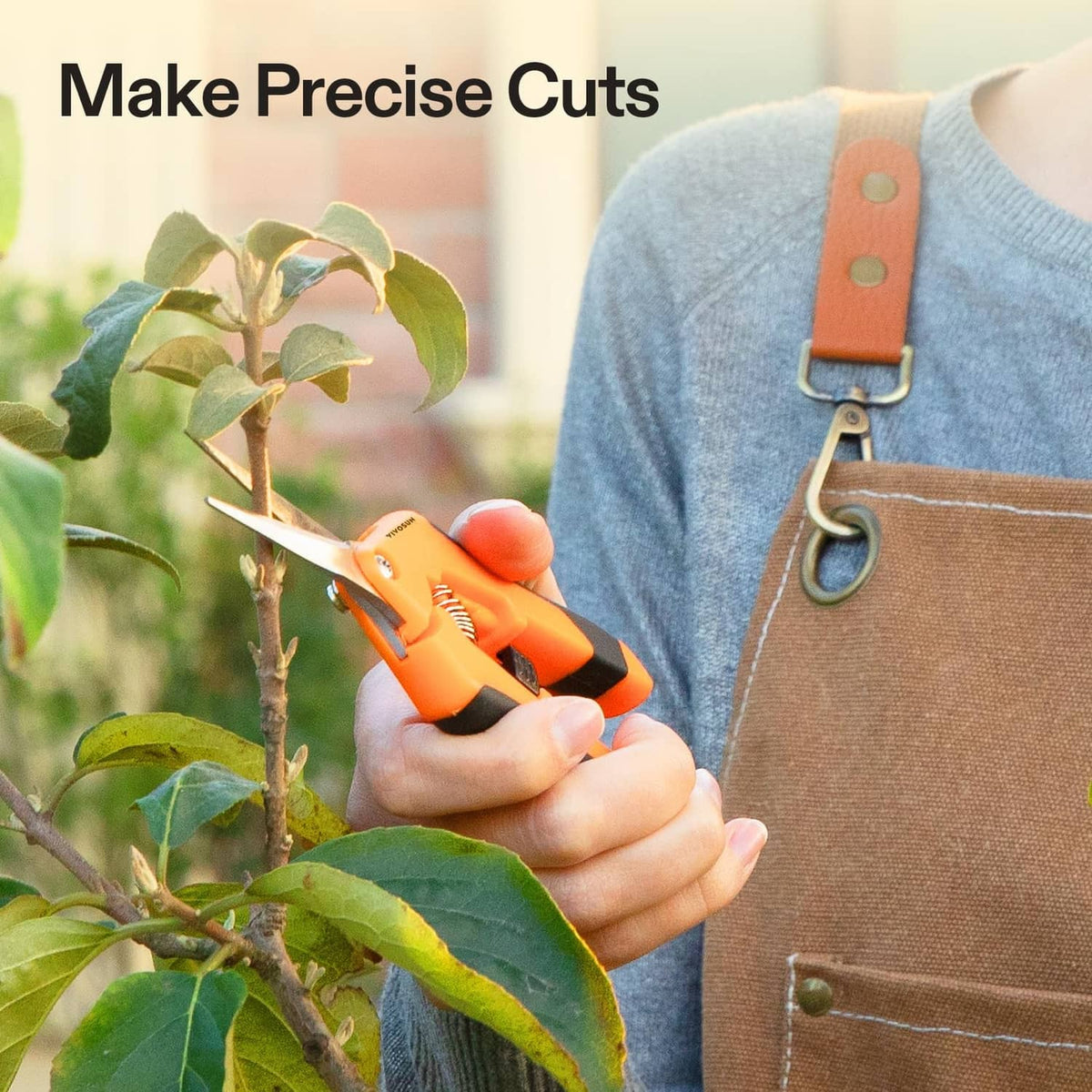Orange pruning shears held in hand trimming small branches on a leafy plant