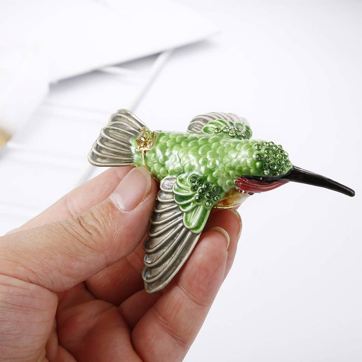 Enamel hummingbird trinket box detail held in hand, green body with silver wings