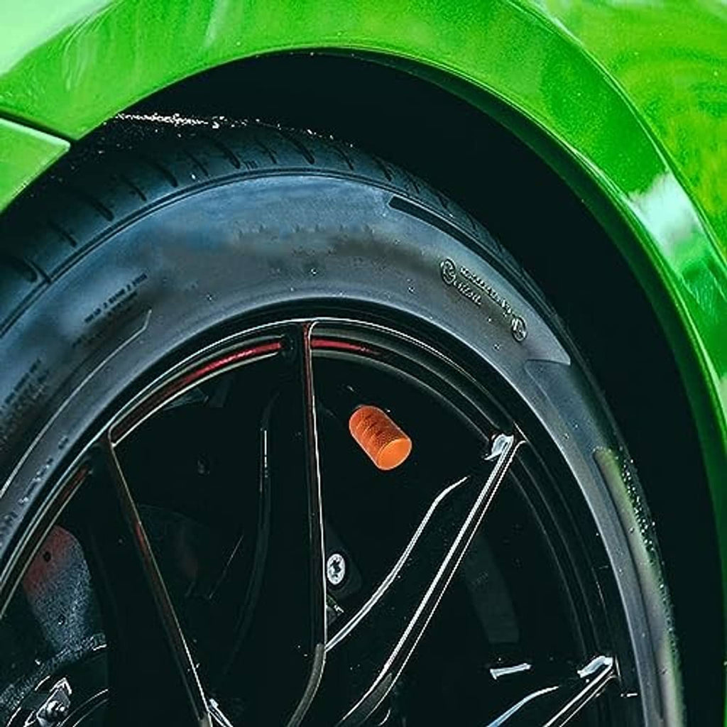 Orange tire valve stem cap installed on black car wheel rim