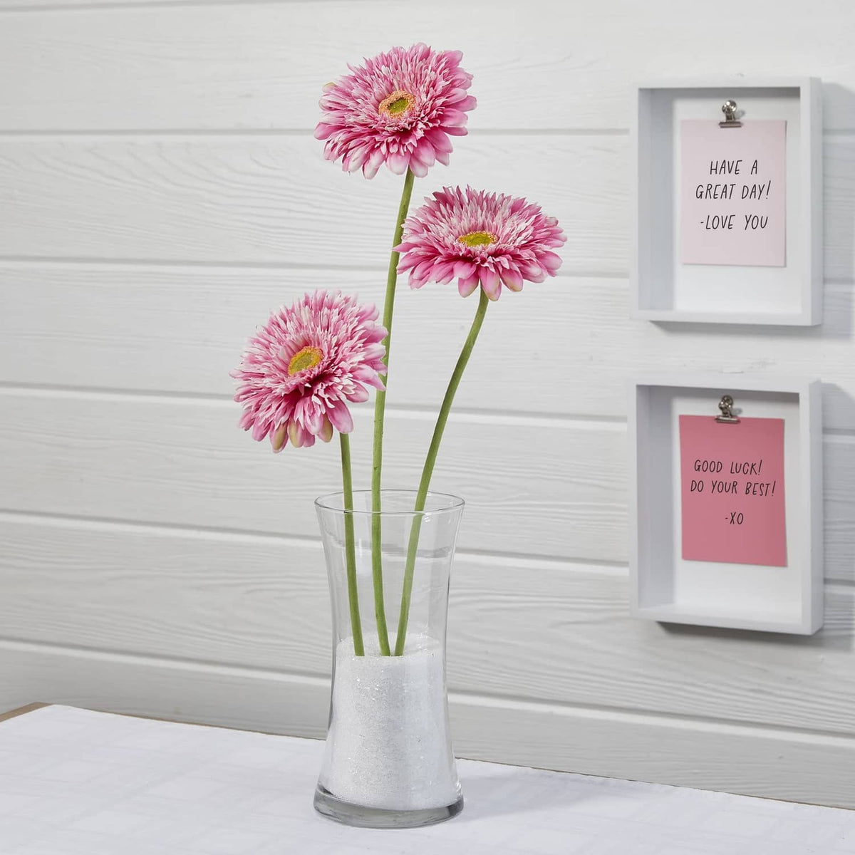 Glitter-coated vase with three pink flowers and green stems, on a white table