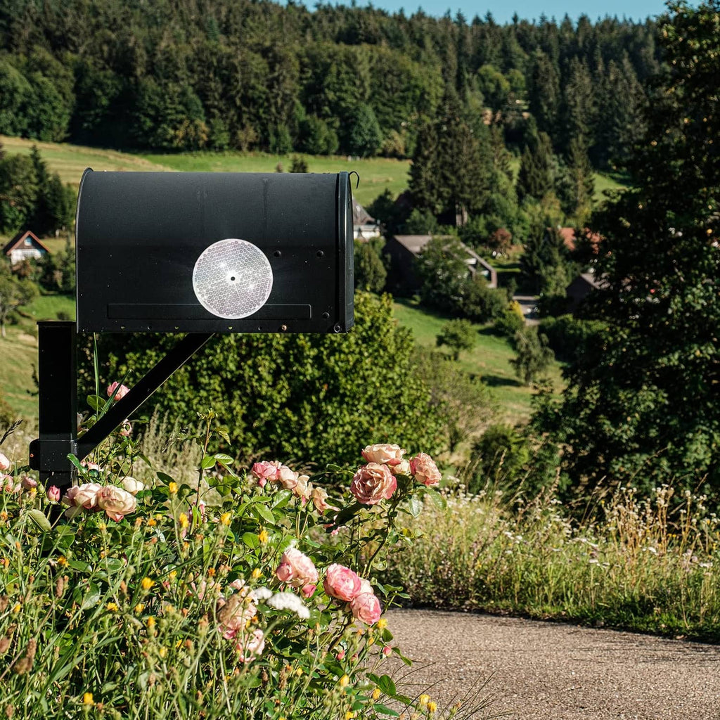 Round white reflective disc mounted on a black fence post for road visibility