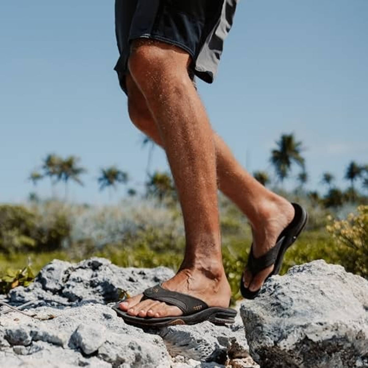 Mens black flip flops worn on rocky ground outdoors