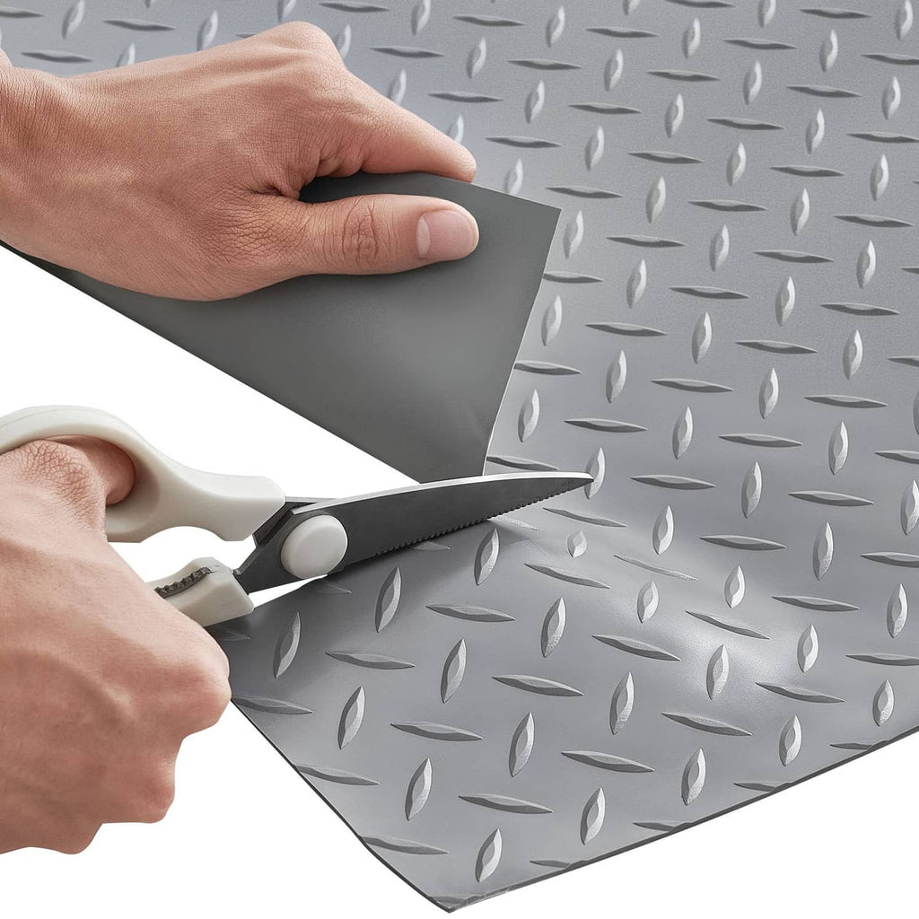 Hands cutting a silver gray PVC diamond-plate garage floor mat to size with scissors.