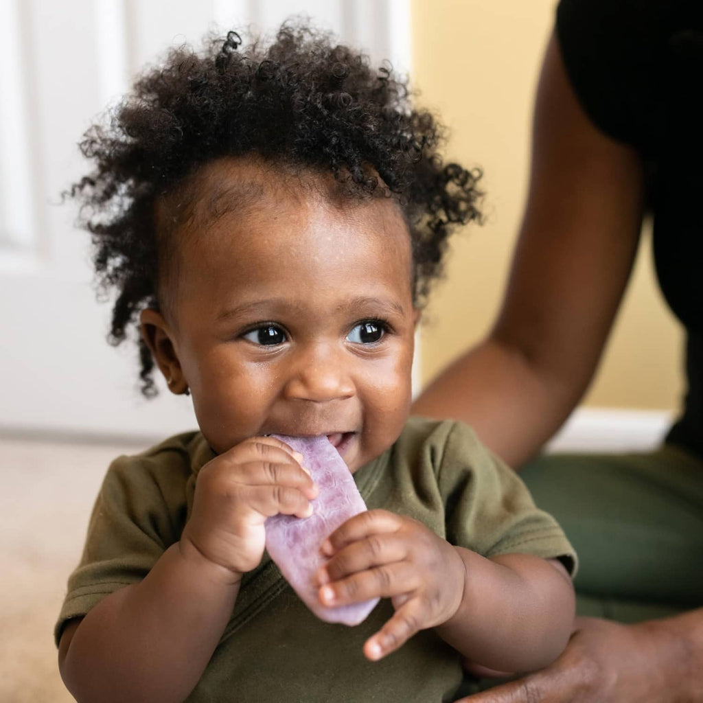 Baby smiling while holding a purple organic teething wafer