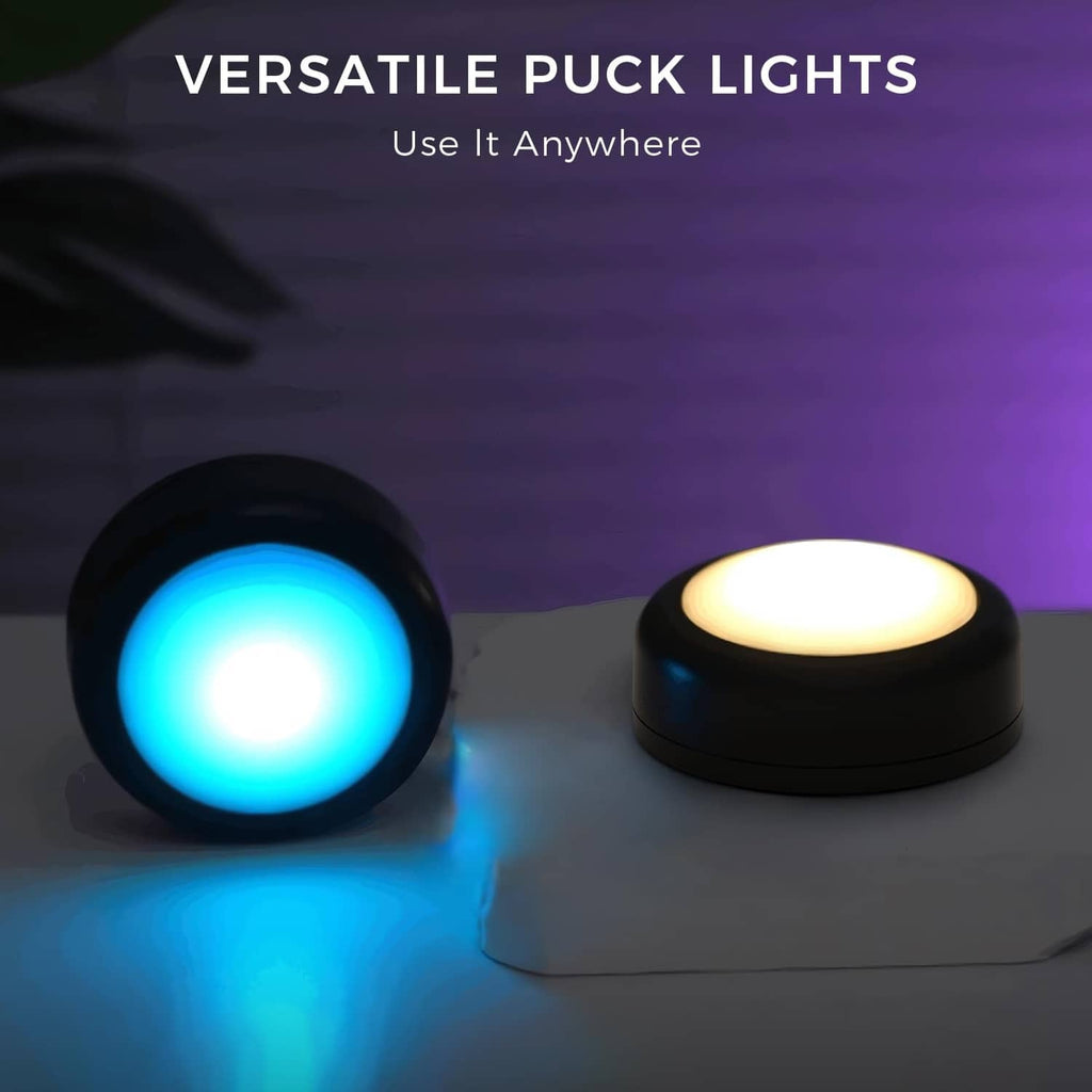 Two black RGB LED puck lights on a surface, one blue and one warm white