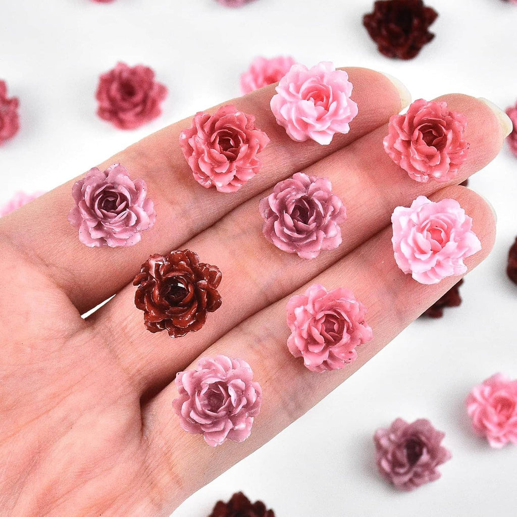 Close-up of tiny peony resin flowers on a hand, pink and dark maroon miniature blossoms