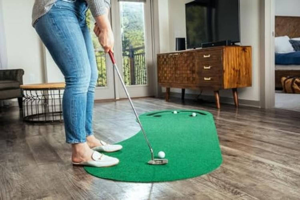 Dark green golf putting green mat with balls and cup holes on a hardwood floor