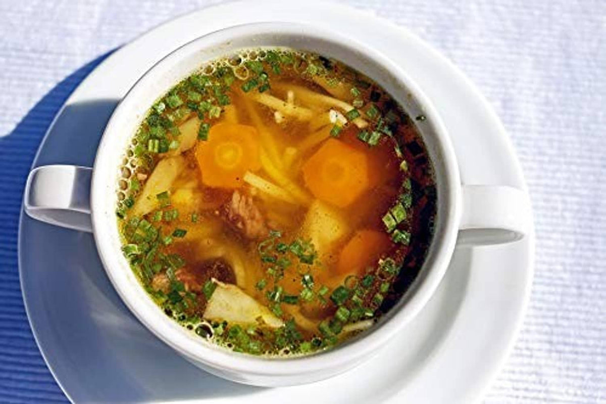 Cup of clear golden soup topped with chopped herbs and diced carrots