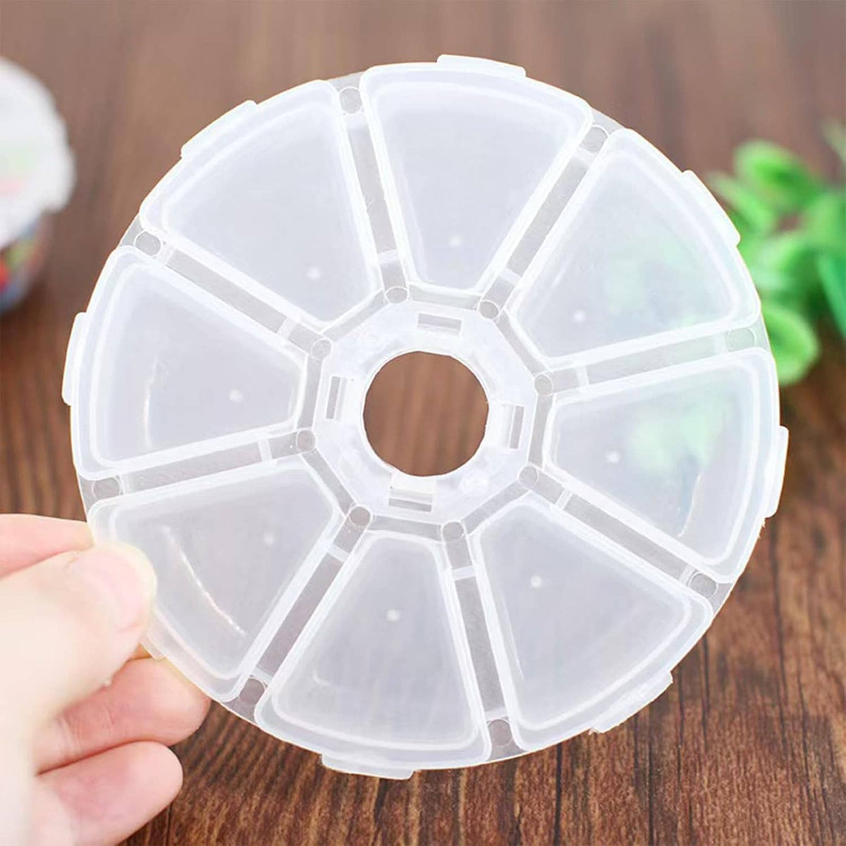 Hand holding a clear round jewelry bead storage box with 8 divided compartments