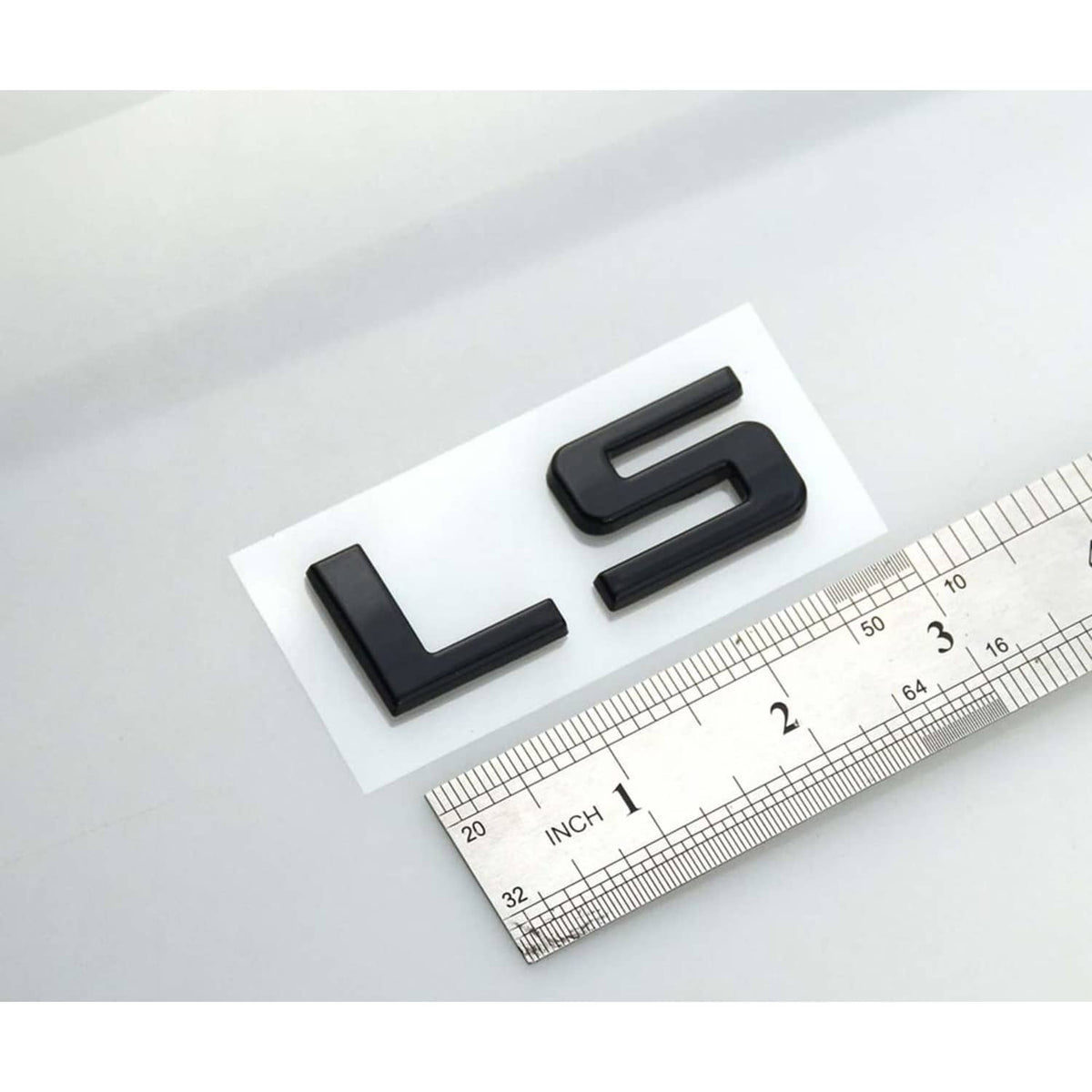 Gloss black LS emblem badge pair with size ruler beside them.