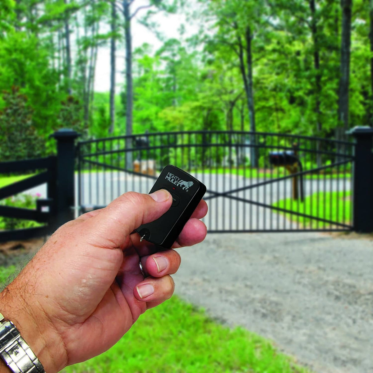 Hand holding a black Mighty Mule gate opener remote by an exterior gate