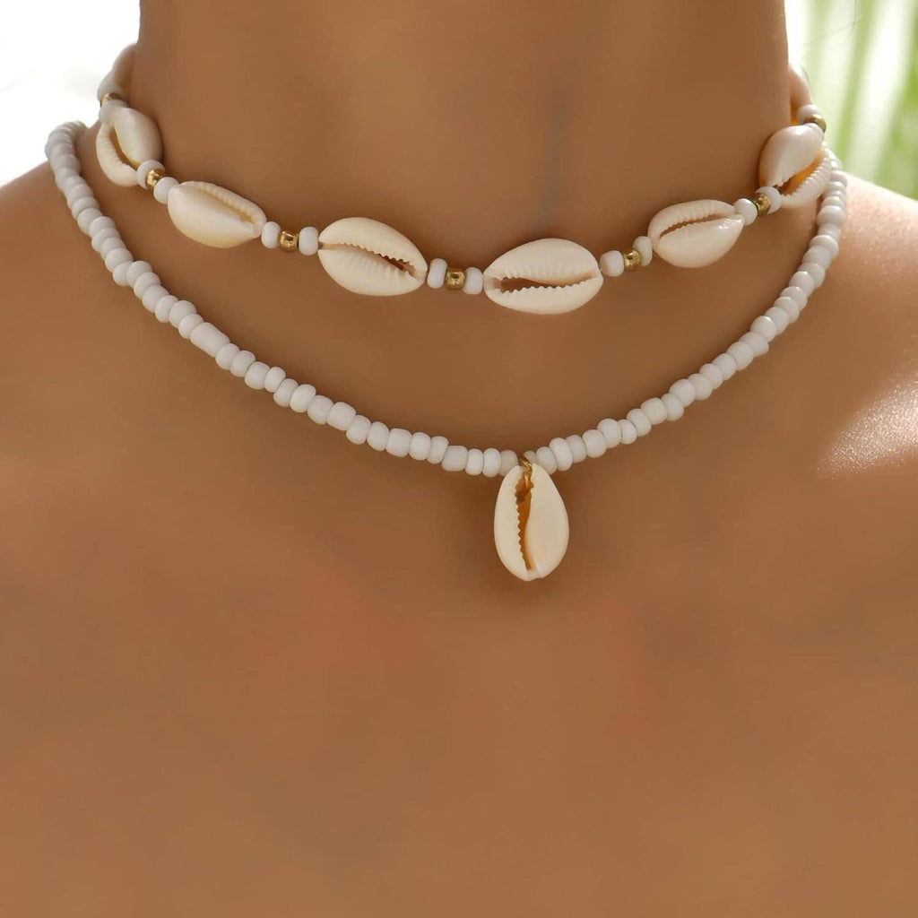 Layered shell necklace with white bead strand and cowrie shells, gold-tone connectors