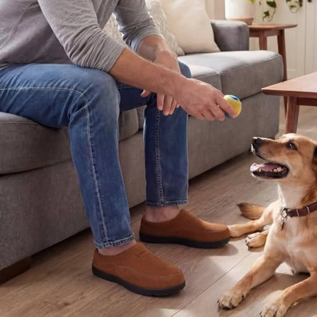 Tan men's slip-on moccasin slippers worn indoors, plush interior and rounded toe
