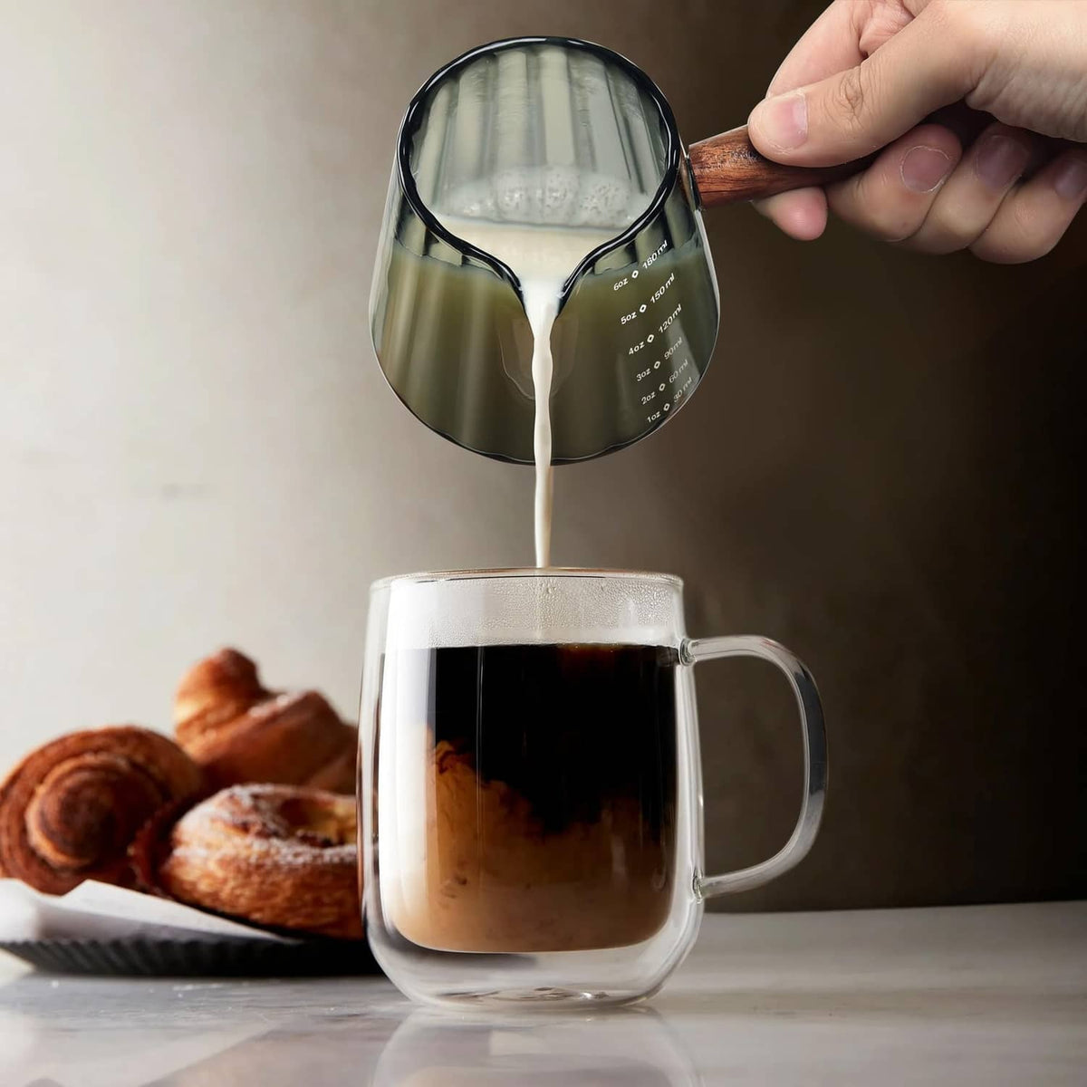 Clear single-spout measuring cup with wood handle pouring into a glass mug