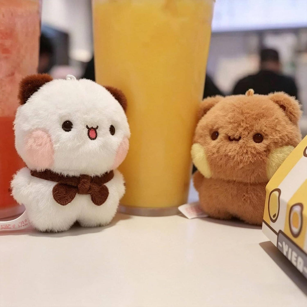 Two small plush bear keychains: white bear and tan bear with brown bow ties