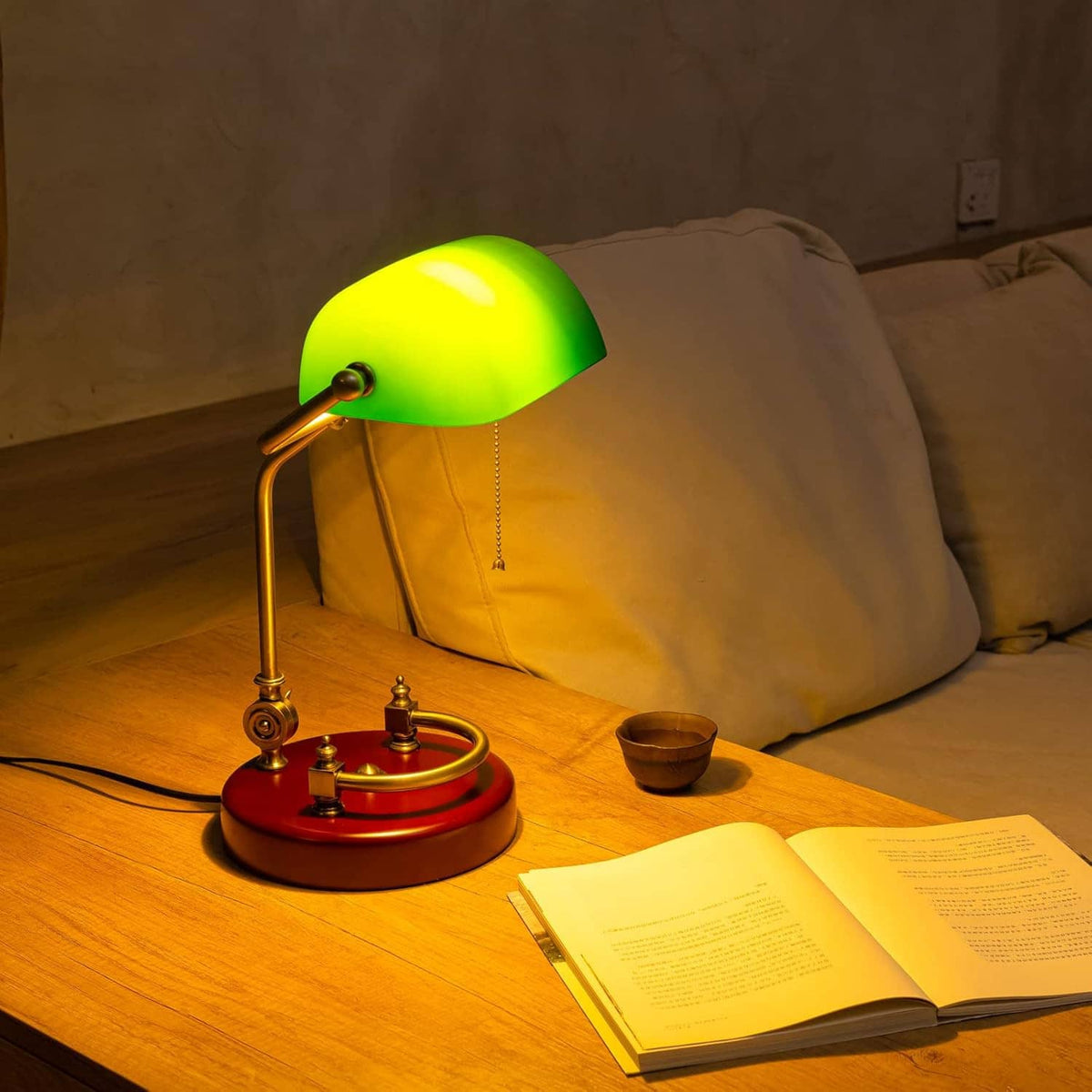 Green glass bankers desk lamp with brass frame and round red base on tabletop