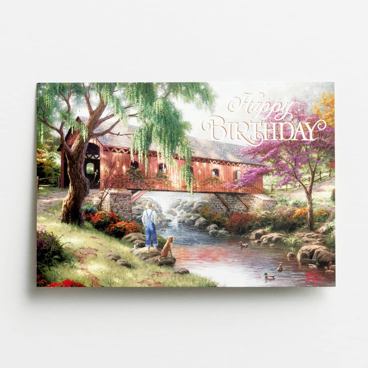 Happy Birthday greeting card with riverside cottage scene and blue-script text