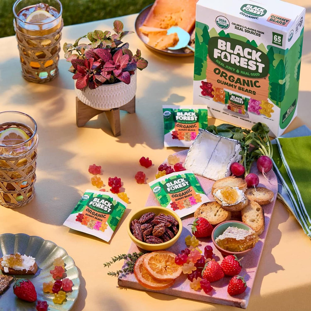 Organic gummy bear pouches with snacks and fruit on a serving board.